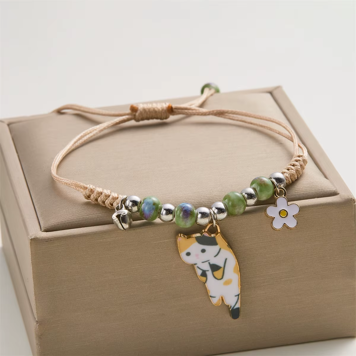 A Heart of Cats cat charm bracelet with green beads resting on a gift box